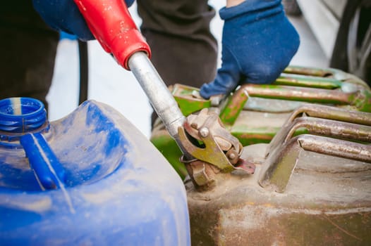 adult man fills a car with petrol at a fuel station in the winter. refueling nozzle man holding in his hand, pouring the liquid in the canister and fuel tank