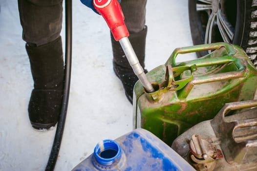 adult man fills a car with petrol at a fuel station in the winter. refueling nozzle man holding in his hand, pouring the liquid in the canister and fuel tank