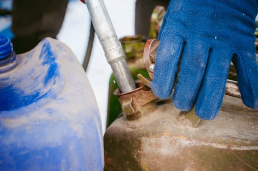 adult man fills a car with petrol at a fuel station in the winter. refueling nozzle man holding in his hand, pouring the liquid in the canister and fuel tank