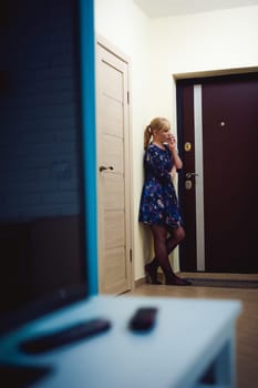 blonde woman answers the intercom call, hold the phone to his ear, waiting for the arrival of the long-awaited guest. Being in apartment near front door