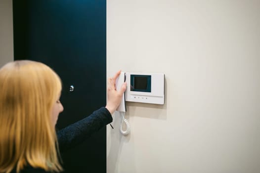 blonde woman hangs up the phone after answering the intercom call in her apartment