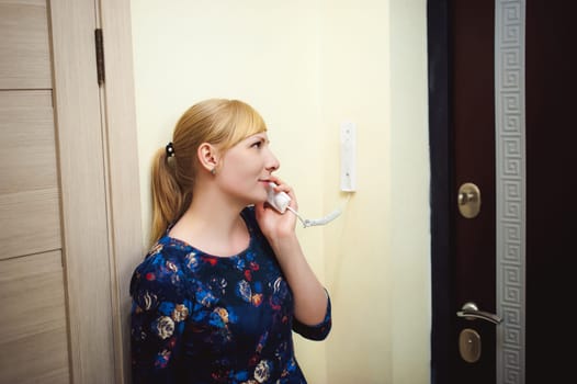 blonde woman answers the intercom call, hold the phone to his ear, waiting for the arrival of the long-awaited guest. Being in apartment near front door