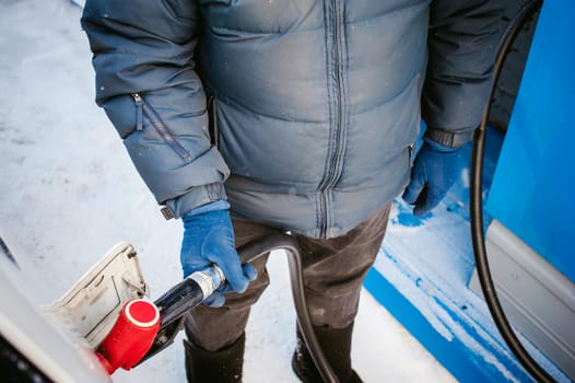 adult man fills a car with petrol at a fuel station in the winter. refueling nozzle man holding in his hand, pouring the liquid in the canister and fuel tank