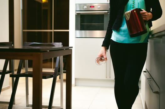 blonde woman in the kitchen holding a glass beaker, pour the water from the kettle to quench their thirst
