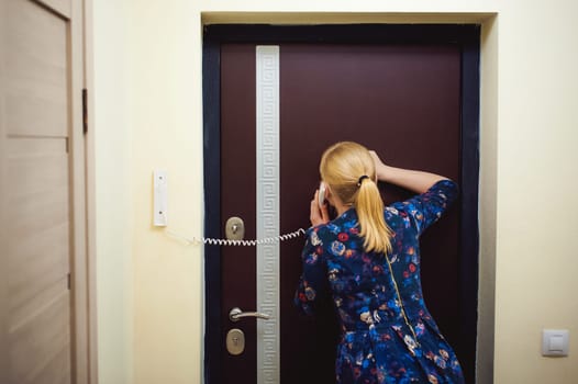 blonde woman answers the intercom call, hold the phone to his ear, waiting for the arrival of the long-awaited guest. Being in apartment near front door
