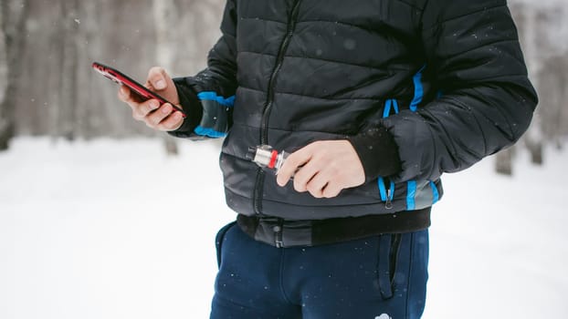 a young man with a beard, smokes an electronic cigarette and happily talking on the phone through the Internet, a positive relaxing outdoors in the snow in the winter