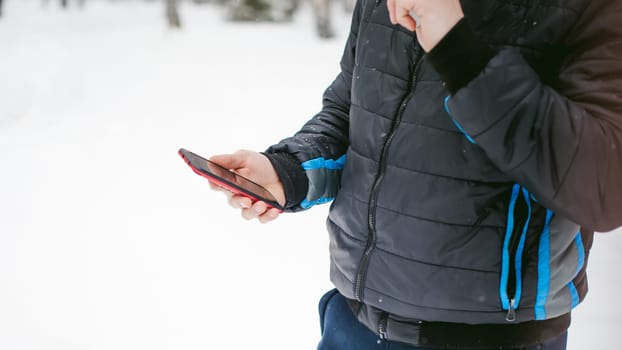 a young man with a beard, smokes an electronic cigarette and happily talking on the phone through the Internet, a positive relaxing outdoors in the snow in the winter