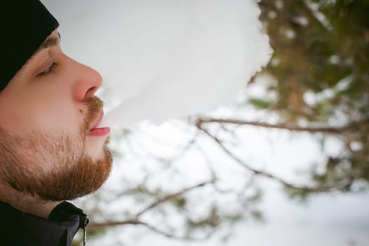 a young man with a beard, smokes an electronic cigarette, outdoors in winter snow