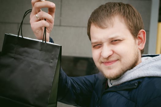 Portrait of a man with a beard with a mustache, holds a package from a store with purchases in his hand, with an emotional face outdoors