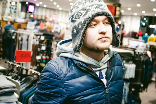 Portrait of a man with a beard with a mustache, putting on winter spring knitted hats in the store, with an emotional face shopping