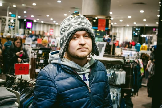 Portrait of a man with a beard with a mustache, putting on winter spring knitted hats in the store, with an emotional face shopping