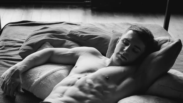 studio portrait young sexy men bodybuilder athlete, with a bare torso, lies on a bed in pillows in underwear