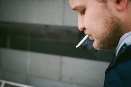 Portrait of a man with a beard with a mustache, smoking a cigarette, with an emotional face in the open air