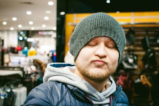 Portrait of a man with a beard with a mustache, putting on winter spring knitted hats in the store, with an emotional face shopping