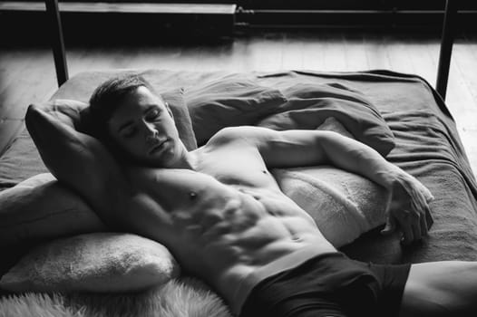 studio portrait young sexy men bodybuilder athlete, with a bare torso, lies on a bed in pillows in underwear