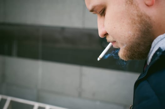Portrait of a man with a beard with a mustache, smoking a cigarette, with an emotional face in the open air