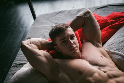 studio portrait young sexy men bodybuilder athlete, with a bare torso, lies on a bed in pillows in underwear