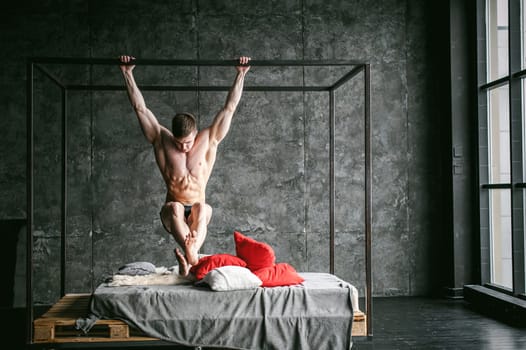 Young sexy men bodybuilder athlete,studio portrait loft on background of stylized wall,guy model With a bare torso pulls up on a horizontal bar on brutal male bed made of metal and pallets
