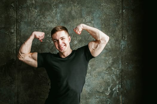 Young sexy men bodybuilder athlete, studio portrait loft on background of stylized Concrete brutal wall, guy model black Tshirt and trousers With powerful muscular arms demonstrates strength