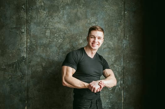 Young sexy men bodybuilder athlete, studio portrait loft on background of stylized Concrete brutal wall, guy model black Tshirt and trousers With powerful muscular arms demonstrates strength