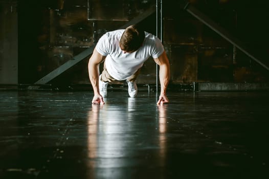 Young sexy male bodybuilder athlete with a bare torso. portrait of a studio of a light-skinned strong man engaged in push-ups on the fists, on the floor, straining powerful hands