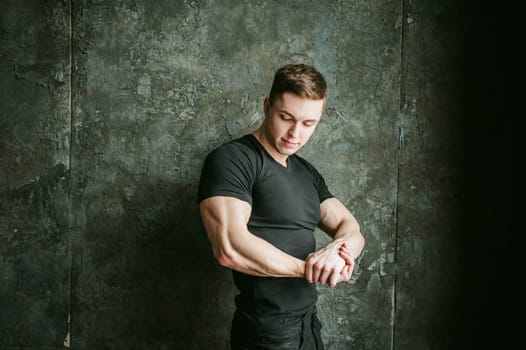 Young sexy men bodybuilder athlete, studio portrait loft on background of stylized Concrete brutal wall, guy model black Tshirt and trousers With powerful muscular arms demonstrates strength