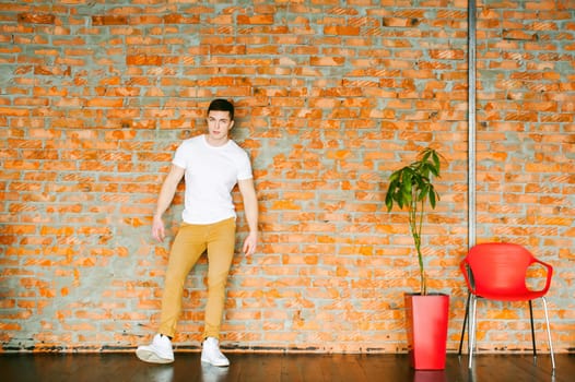 Young sexy men bodybuilder athlete,studio portrait in loft, guy model in white T-shirt and brown trousers, Leaned against a brick wall