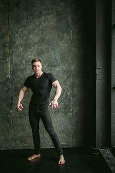 Young sexy men bodybuilder athlete, studio portrait loft on background of stylized Concrete brutal wall, guy model black Tshirt and trousers