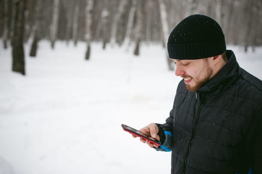 a young man with a beard, smokes an electronic cigarette and happily talking on the phone through the Internet, a positive relaxing outdoors in the snow in the winter