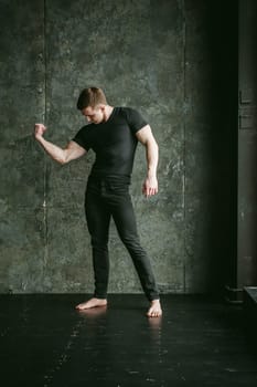 Young sexy men bodybuilder athlete, studio portrait loft on background of stylized Concrete brutal wall, guy model black Tshirt and trousers With powerful muscular arms demonstrates strength