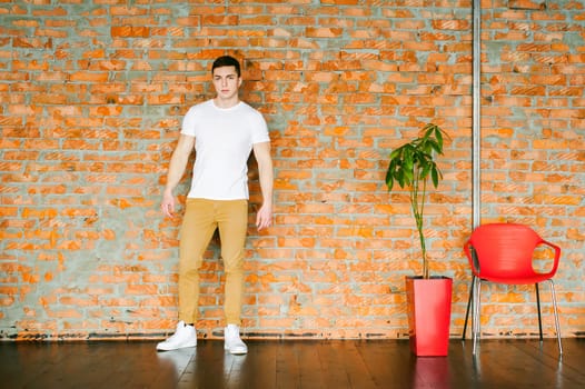 Young sexy men bodybuilder athlete,studio portrait in loft, guy model in white T-shirt and brown trousers, Leaned against a brick wall