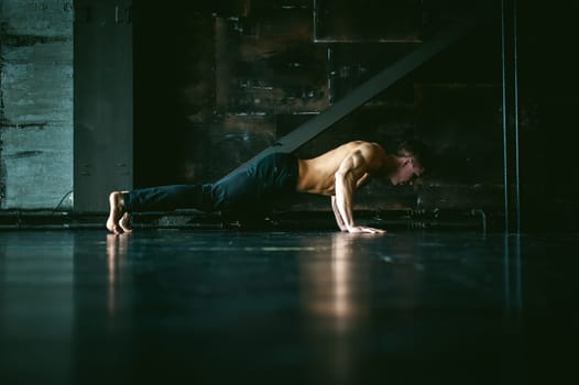 Young sexy male bodybuilder athlete with a bare torso. portrait of a studio of a light-skinned strong man engaged in push-ups, on the floor, straining powerful hands