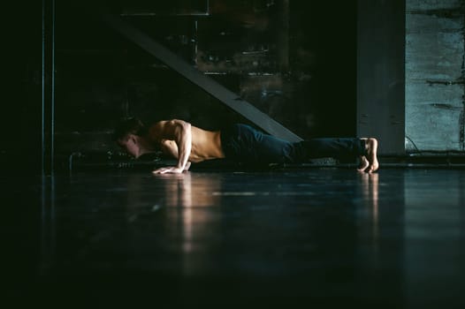 Young sexy male bodybuilder athlete with a bare torso. portrait of a studio of a light-skinned strong man engaged in push-ups, on the floor, straining powerful hands