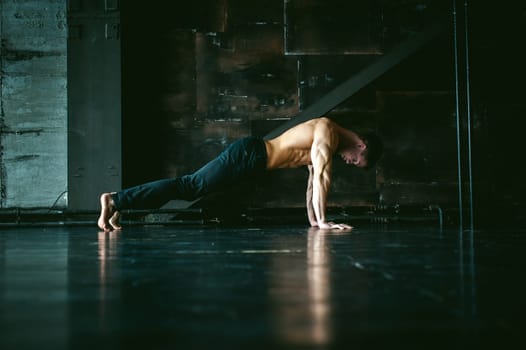 Young sexy male bodybuilder athlete with a bare torso. portrait of a studio of a light-skinned strong man engaged in push-ups, on the floor, straining powerful hands
