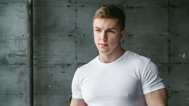 Young sexy men bodybuilder athlete,studio portrait in loft on the background of stylized wall and Black leather sofa, guy model in white T-shirt and brown trousers against background of larger window