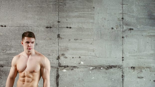 Young sexy men bodybuilder athlete with a naked torso against the background of a gray wall, studio portrait