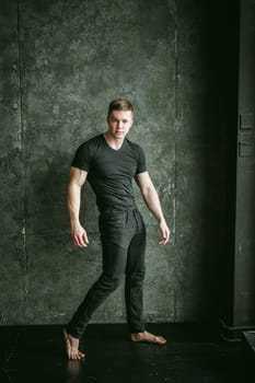Young sexy men bodybuilder athlete, studio portrait loft on background of stylized Concrete brutal wall, guy model black Tshirt and trousers