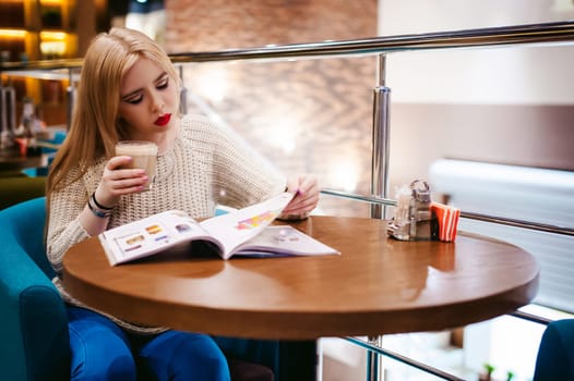 Picture of young lady sitting in cafe while reading magazine And drinks coffee