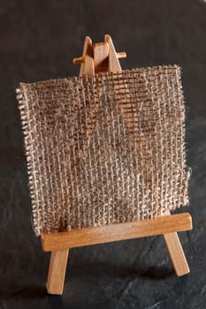 Elevated view of a mini easel with coarse linen fabric as a painting surface against a dark background on slate plate.