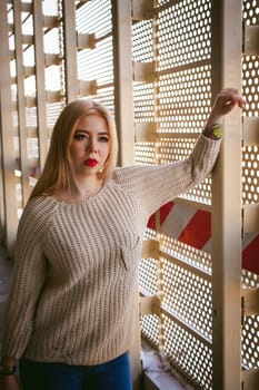 Portrait of a young woman dressed in a knitted sweater and blue jeans. Standing near a metal perforated parking fence construction