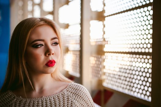 Portrait of a young woman dressed in a knitted sweater and blue jeans. Standing near a metal perforated parking fence construction