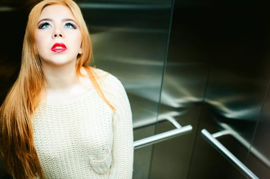 Portrait of a female face, young blond woman with plump lips and beautiful eyes dressed in a knitted sweater. Against elevator lift background