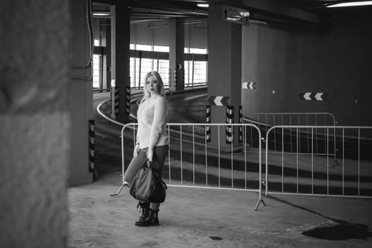 Portrait of a young woman dressed in a knitted sweater and blue jeans, holds in her hand a sports bag. standing on the background of a climb to the parking floor