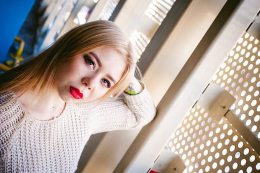 Portrait of a young woman dressed in a knitted sweater and blue jeans. Standing near a metal perforated parking fence construction