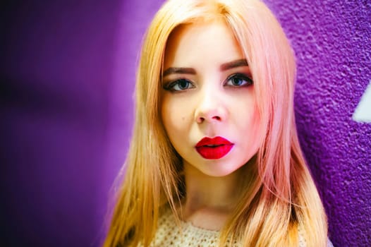 Close-up portrait of a female face, young blonde woman with plump lips and beautiful eyes. Against the background of a lilac relief wall