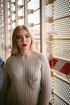 Portrait of a young woman dressed in a knitted sweater and blue jeans. Standing near a metal perforated parking fence construction