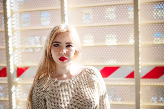 Portrait of a young woman dressed in a knitted sweater and blue jeans. Standing near a metal perforated parking fence construction
