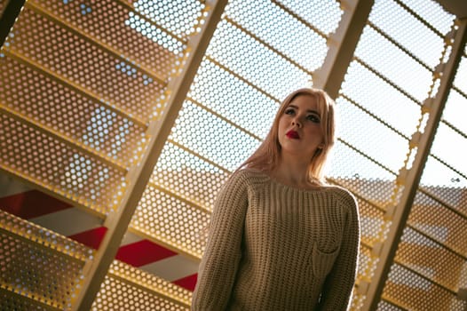 Portrait of a young woman dressed in a knitted sweater and blue jeans. Standing near a metal perforated parking fence construction
