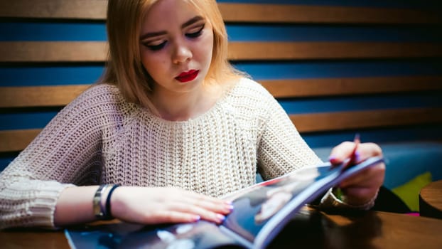 Picture of young lady sitting in cafe while reading magazine.