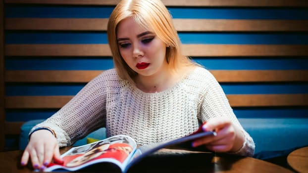 Picture of young lady sitting in cafe while reading magazine.